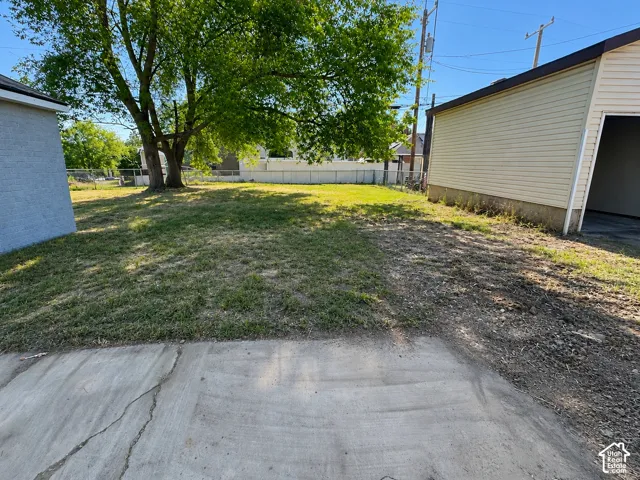 Expansive yard space featuring a mature tree, concrete pad, and a detached garage with horizontal siding