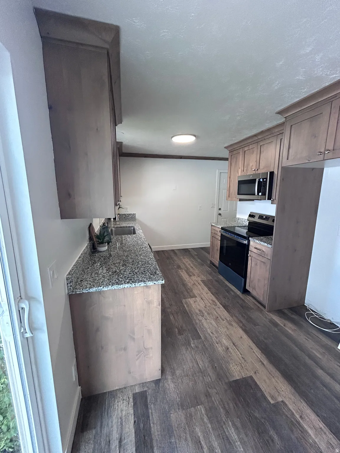 Kitchen featuring wood-finish flooring, wood cabinetry with crown molding, granite-style countertops, and stainless steel appliances including a built-in microwave and range