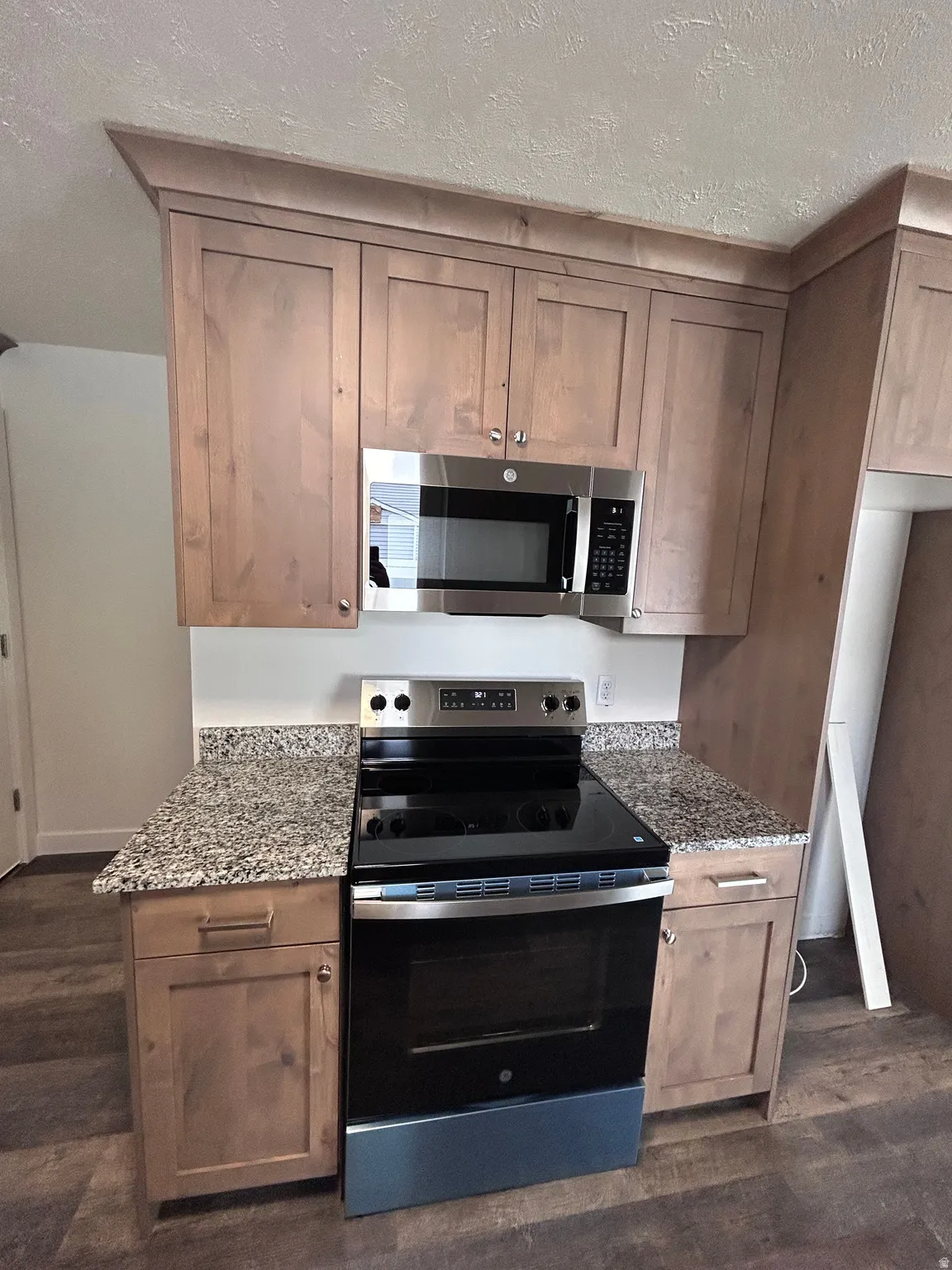 Modern kitchen featuring wood-finish cabinetry, granite-patterned countertops, stainless steel appliances, and wood-finish flooring