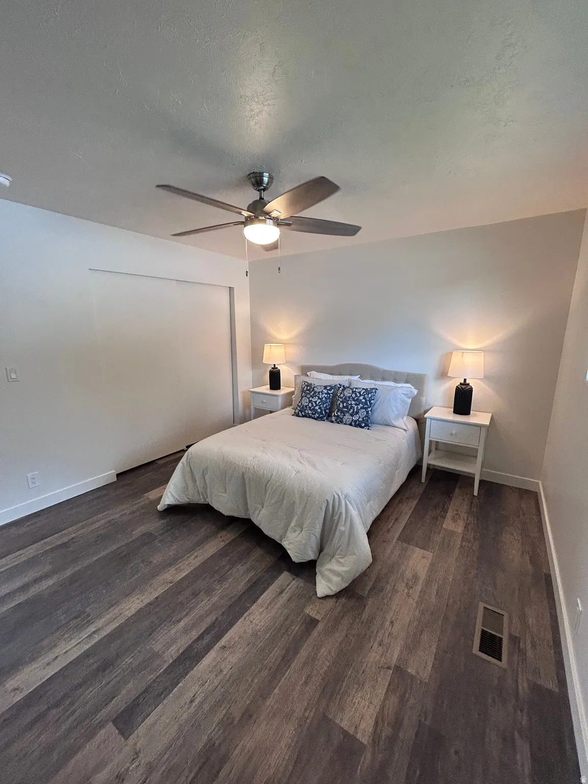 Wood-finish flooring throughout, featuring a ceiling fan with integrated lighting, white baseboards, and a built-in closet with sliding doors