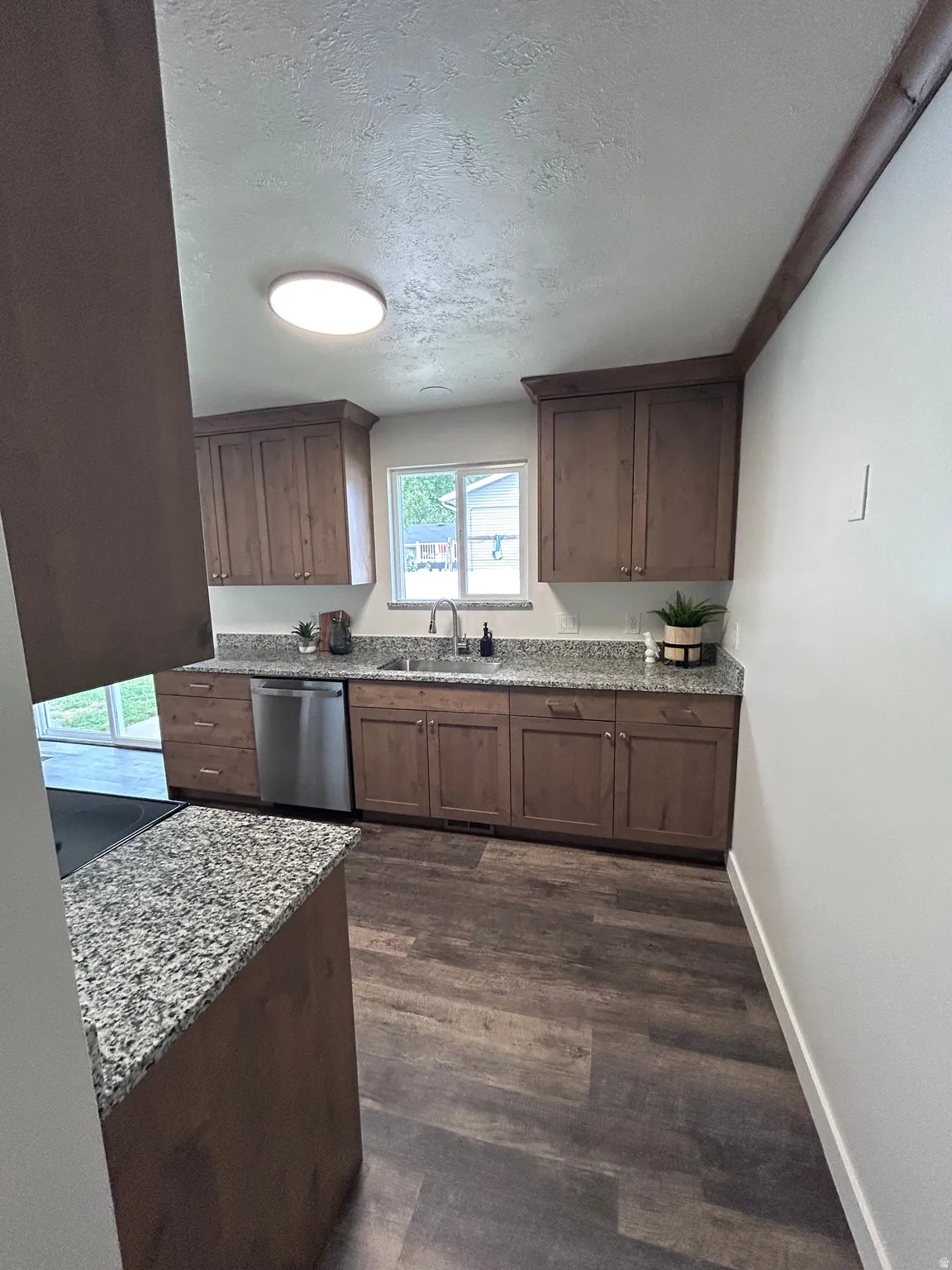 Kitchen featuring wood-finish cabinetry, granite-style countertops, stainless steel dishwasher, and wood-look flooring