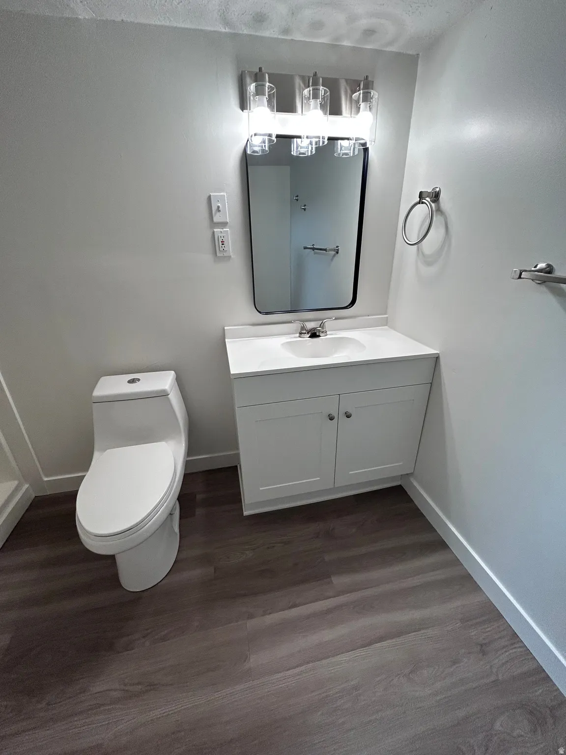Bathroom featuring a white vanity with integrated sink, contemporary mirror, and a three-light vanity fixture