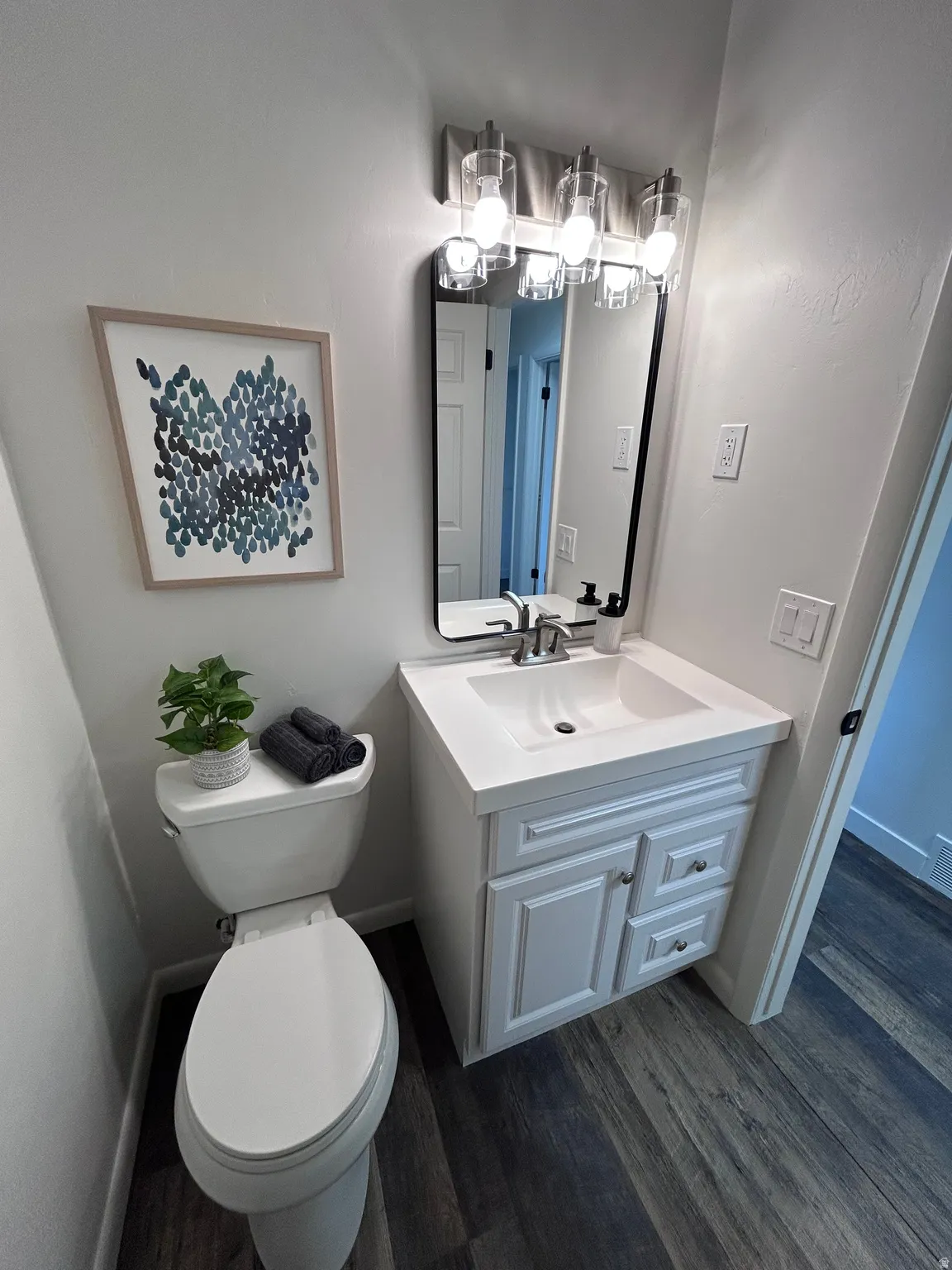 Bathroom featuring a single vanity with a white countertop and integrated sink, a frameless rectangular mirror, and a three-light vanity fixture