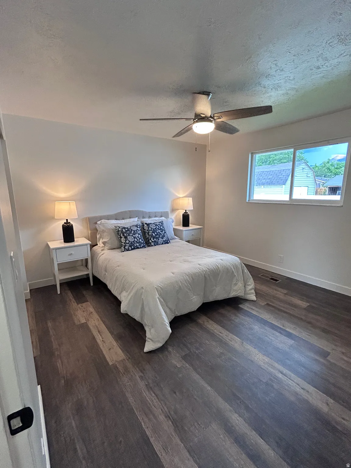 Spacious bedroom featuring wood-finish flooring, a multi-pane window, and a ceiling fan with integrated lighting