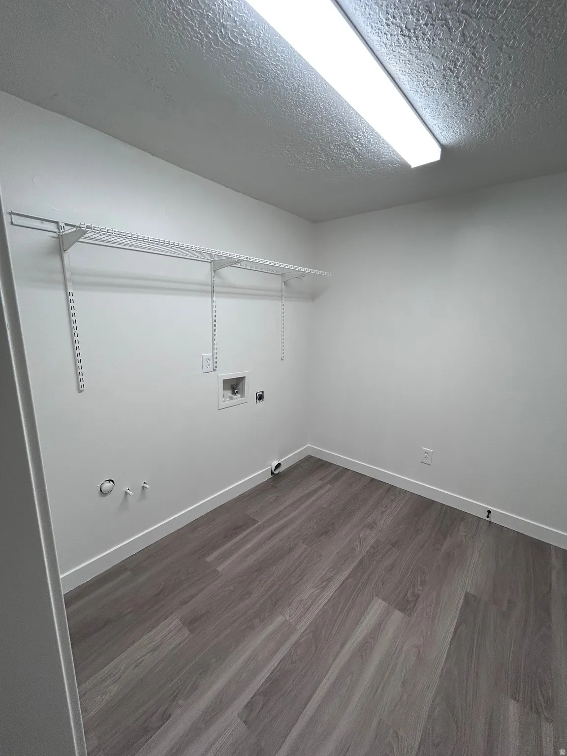 Laundry area featuring wood-finish flooring, white walls, and built-in wire shelving