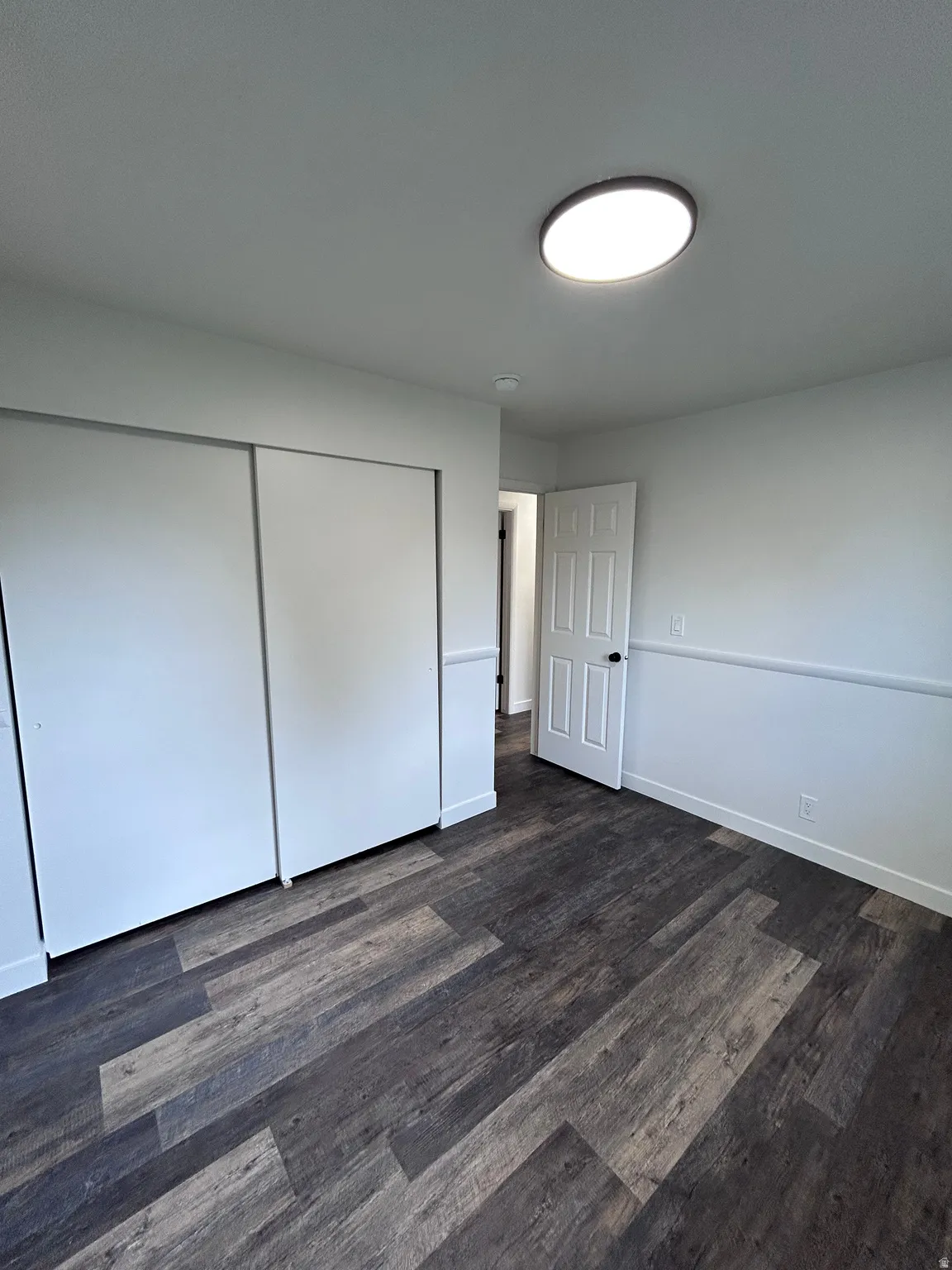 Room featuring wood-finish flooring, white walls with wainscoting, and a flush-mount ceiling light