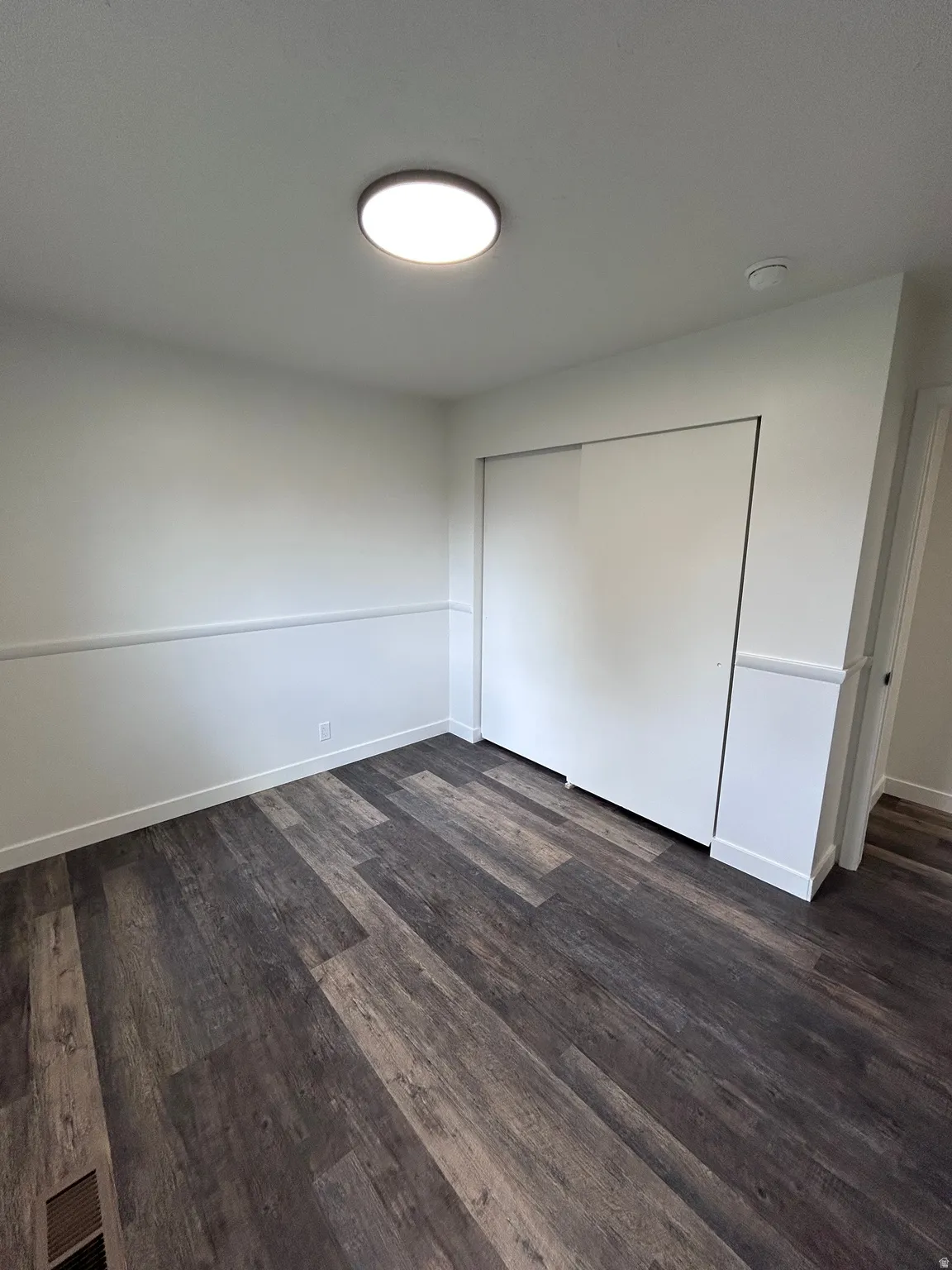 Spacious room featuring wood-finish flooring, white walls with wainscoting, and a ceiling-mounted flush light fixture
