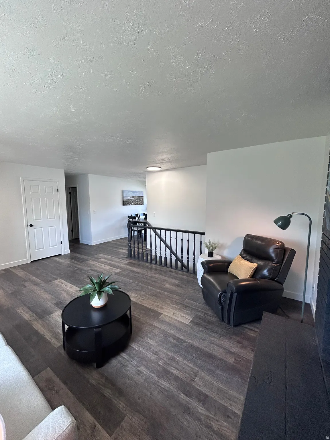 Spacious living area featuring wood-finish flooring, white walls, and a black painted fireplace hearth