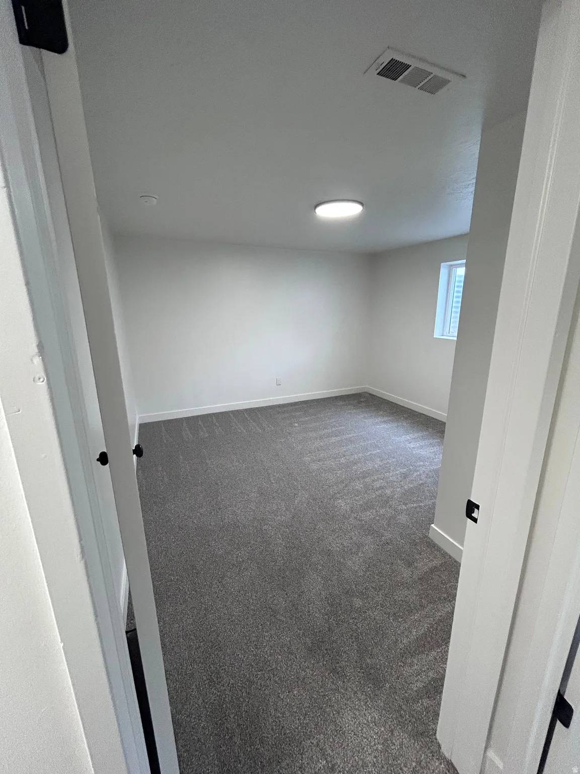 Spacious room featuring gray textured carpeting, white walls, and a contemporary ceiling light fixture