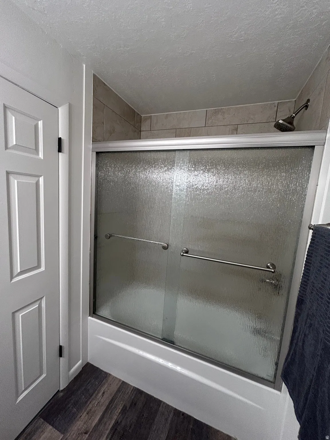 Bathtub with textured glass shower enclosure, brushed nickel shower head, and tile surround