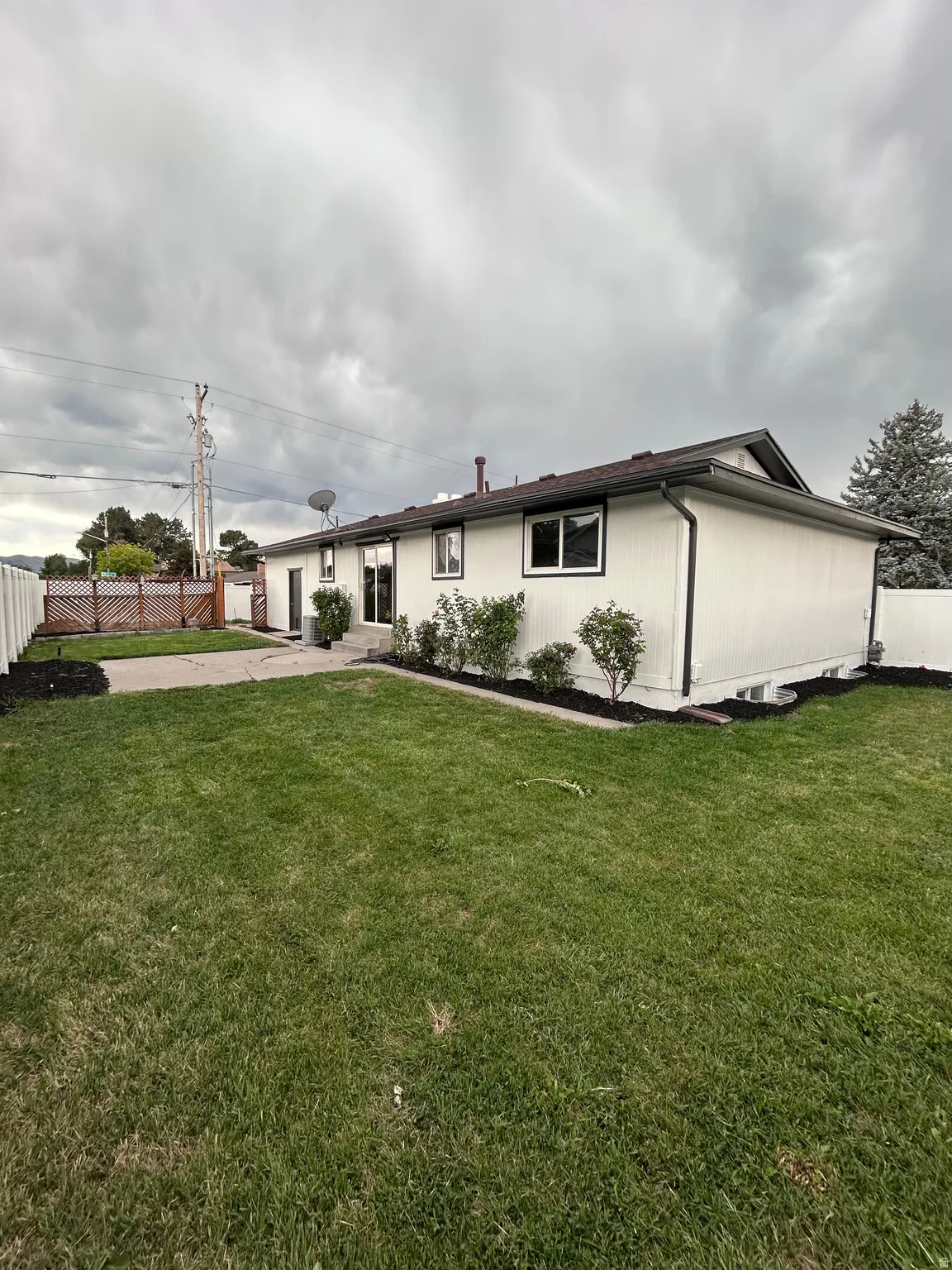 Expansive green lawn with a white vinyl fence and a concrete patio