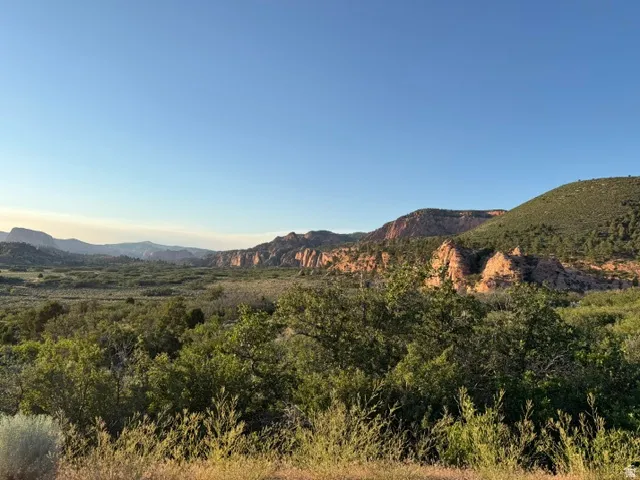 Expansive natural landscape featuring distant red rock formations and verdant rolling hills