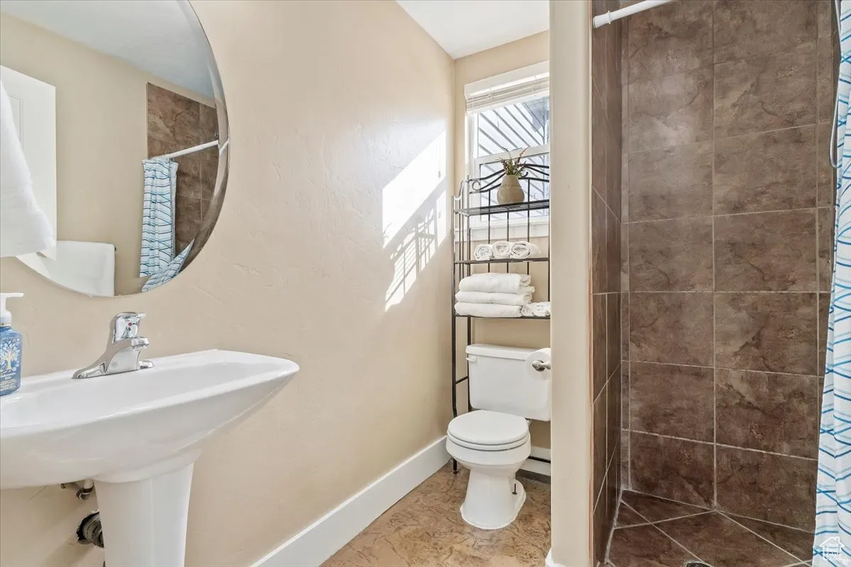 2nd Main Floor Bathroom featuring a pedestal sink with chrome faucet, an oval wall-mounted mirror, and a walk-in shower with brown tiled walls and floor
