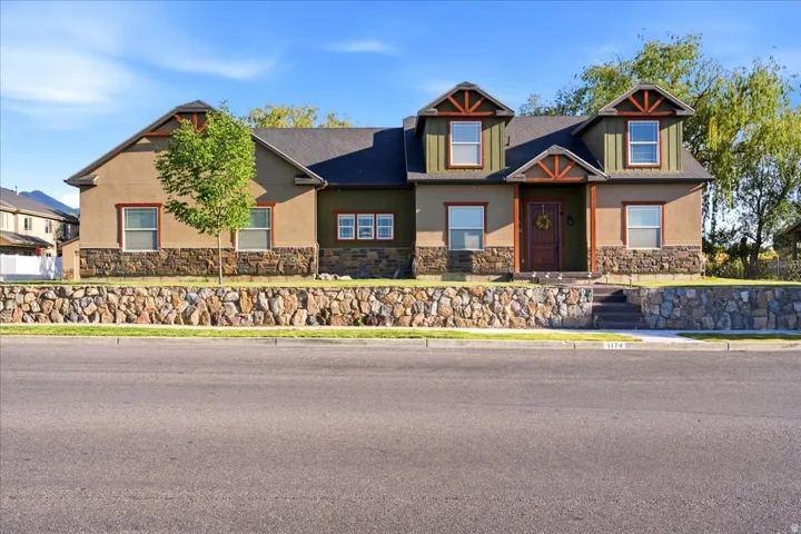 Multi-level residence featuring a prominent stone retaining wall, stucco siding, and dark trim accents