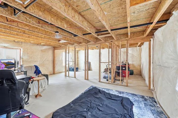 Unfinished lower level featuring exposed wood joists and subfloor, partial insulation, structural wood framing for future rooms, and a concrete floor