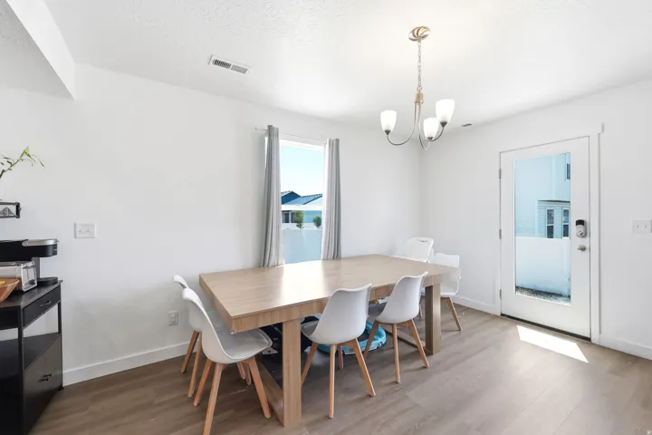 Open-concept dining area featuring a contemporary chandelier, large window with natural light, and a glass-paneled exterior door