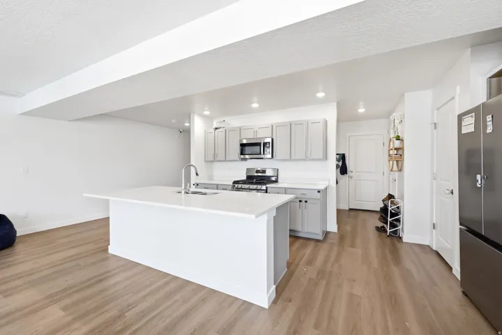 Kitchen featuring a large island with white countertop, light grey cabinetry, stainless steel appliances, and wood-finish flooring