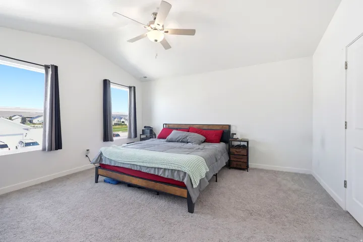 Spacious room featuring vaulted ceilings, two large windows, a ceiling fan, and carpeted flooring