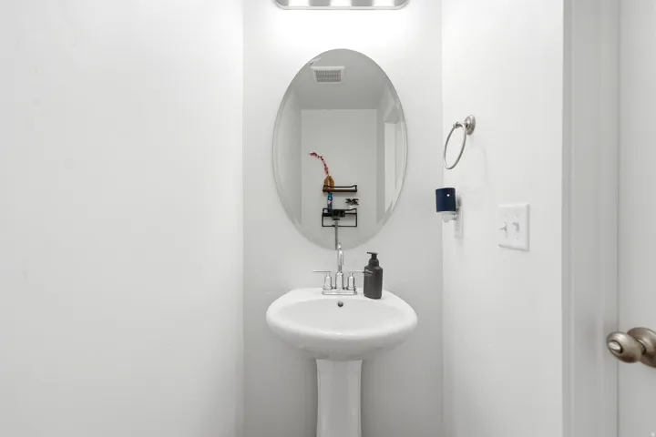 Pedestal sink with an oval mirror and a wall-mounted light fixture