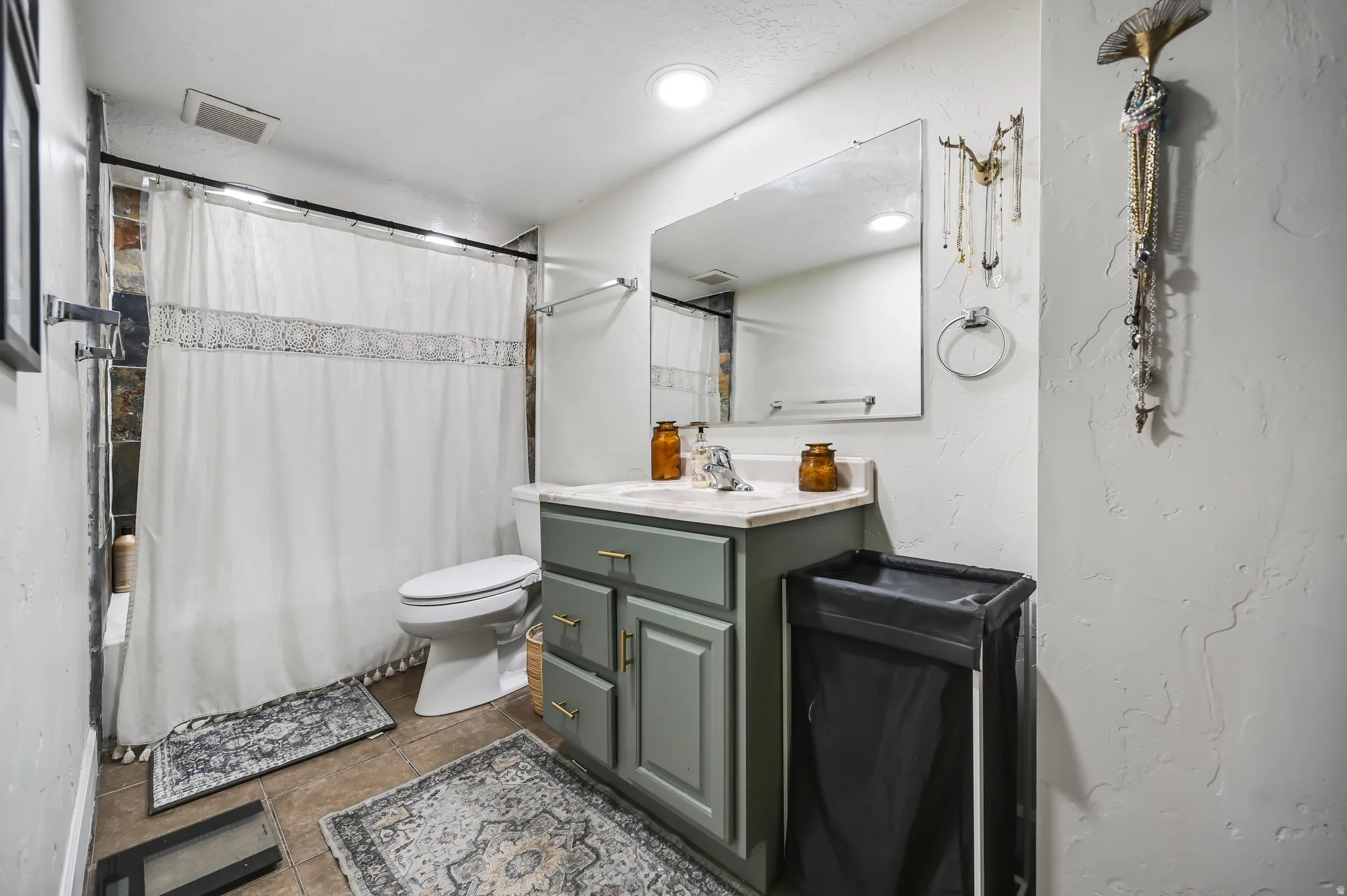 Full bathroom featuring a single vanity with a light countertop, a rectangular mirror, and a shower-over-tub combination with stone-look tile surround