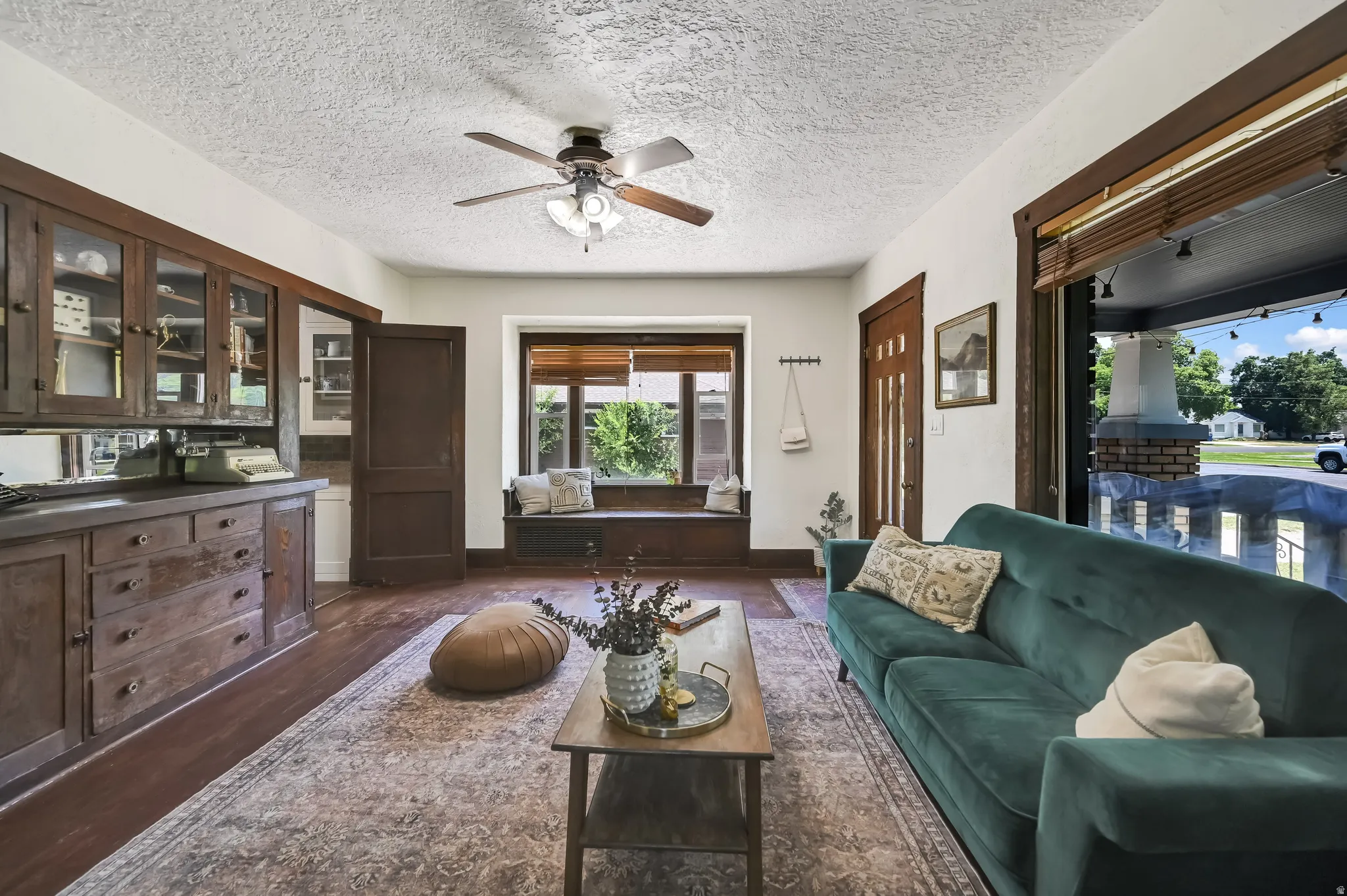 Living area featuring wood-finish flooring, built-in cabinetry with glass fronts, a window seat, exposed wood trim, and a ceiling fan light fixture