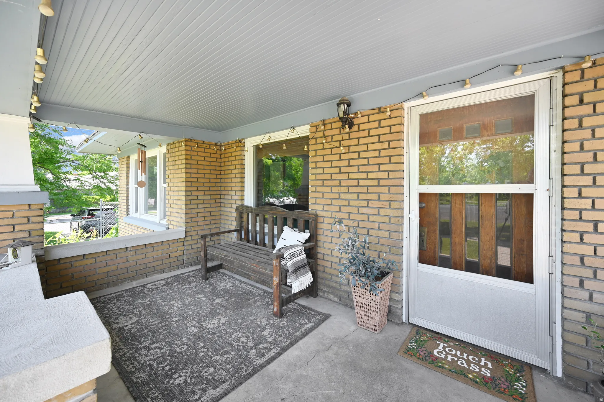 Covered front porch featuring brick siding, a concrete floor, and a beadboard ceiling