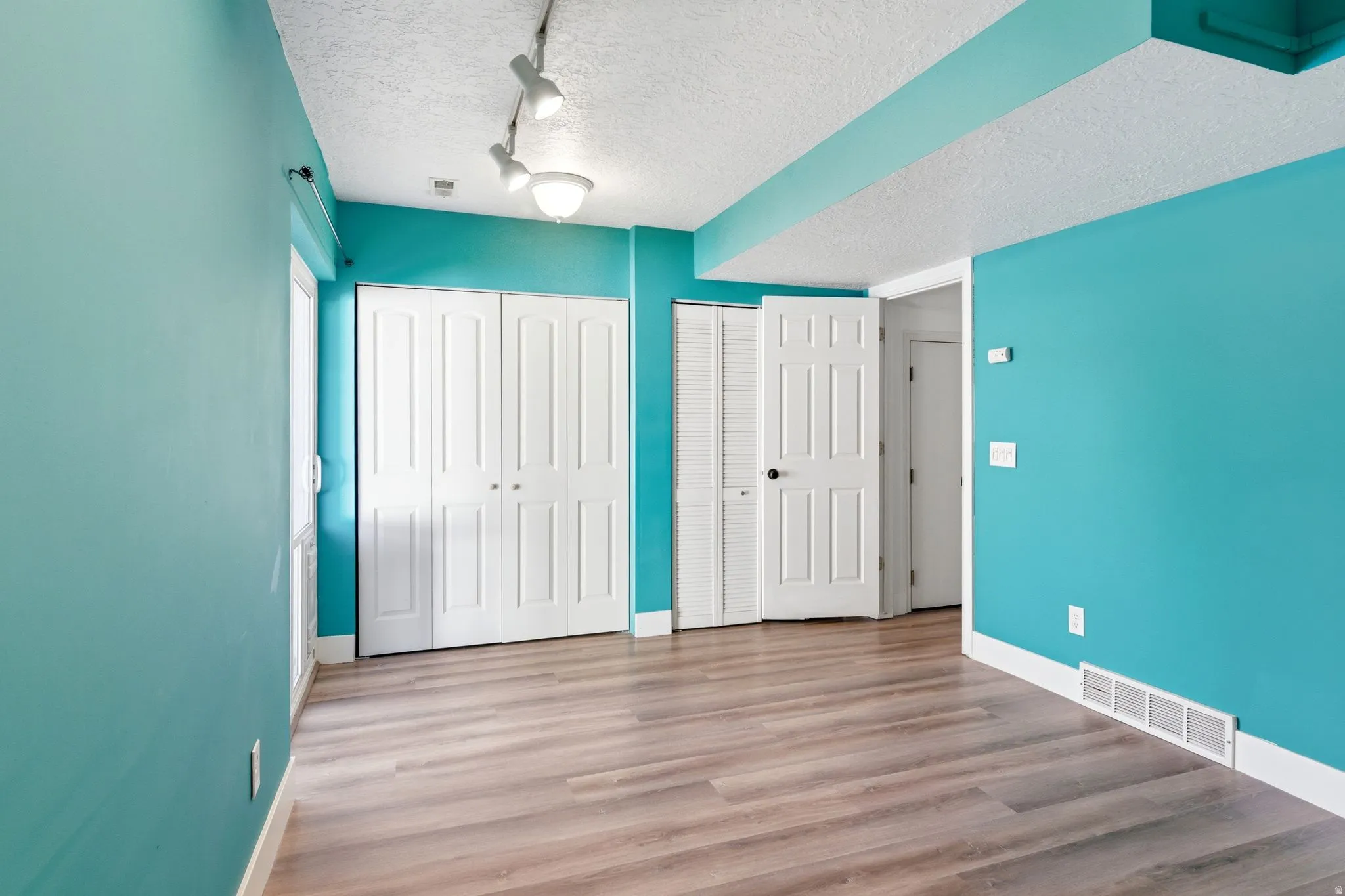 Interior space featuring wood-finish flooring, white baseboards, and vibrant teal walls