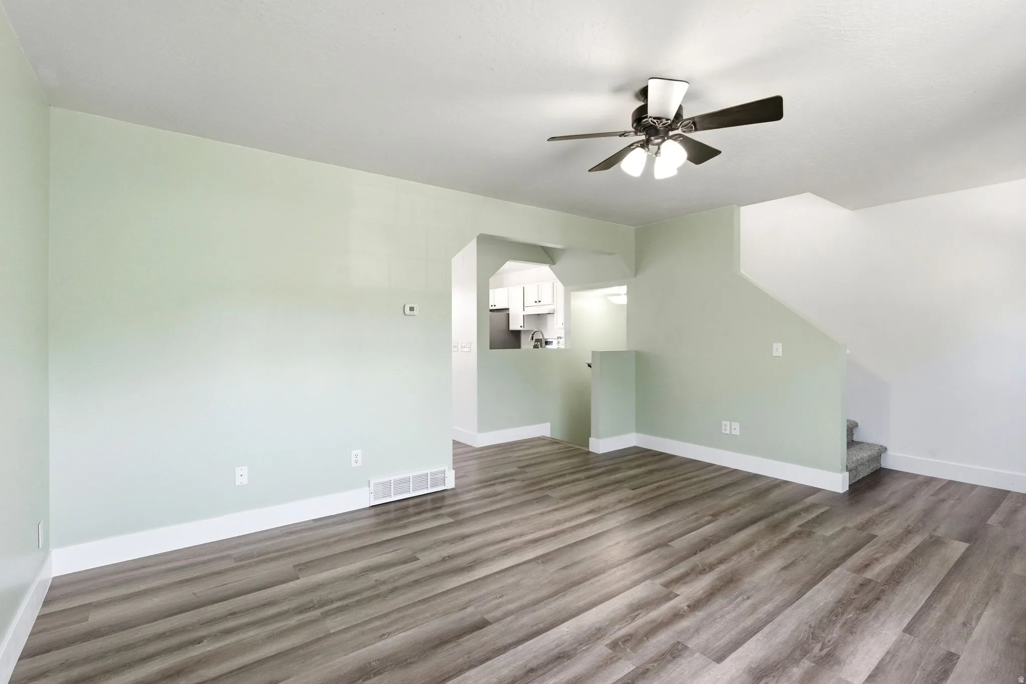 Spacious interior featuring wood-finish flooring, a ceiling fan with integrated lighting, and a staircase with carpeted treads