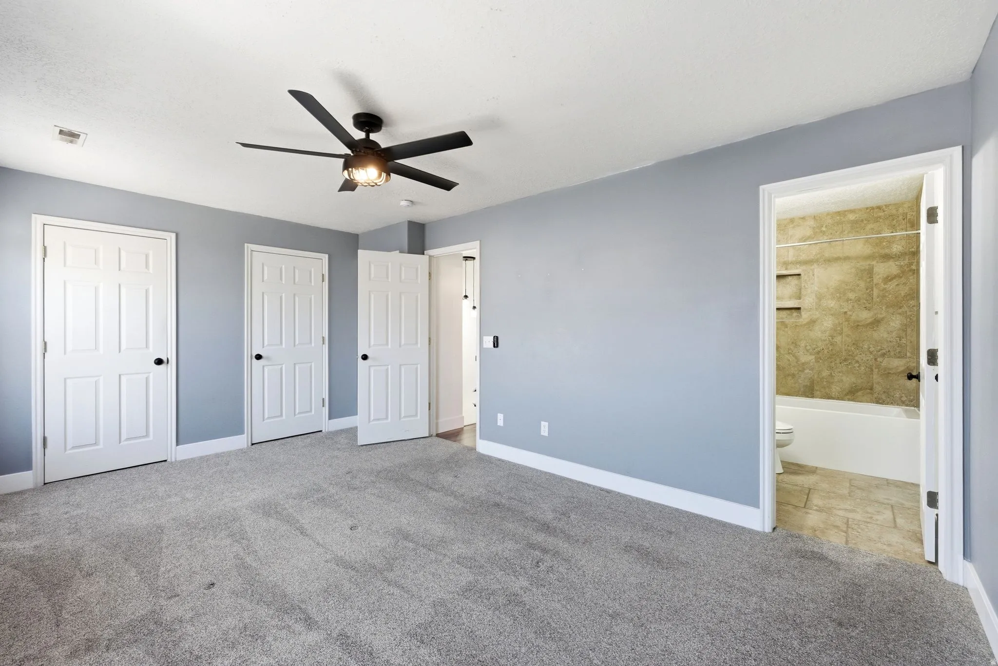 Spacious room featuring light gray carpeting, light blue walls, and a ceiling fan with integrated lighting