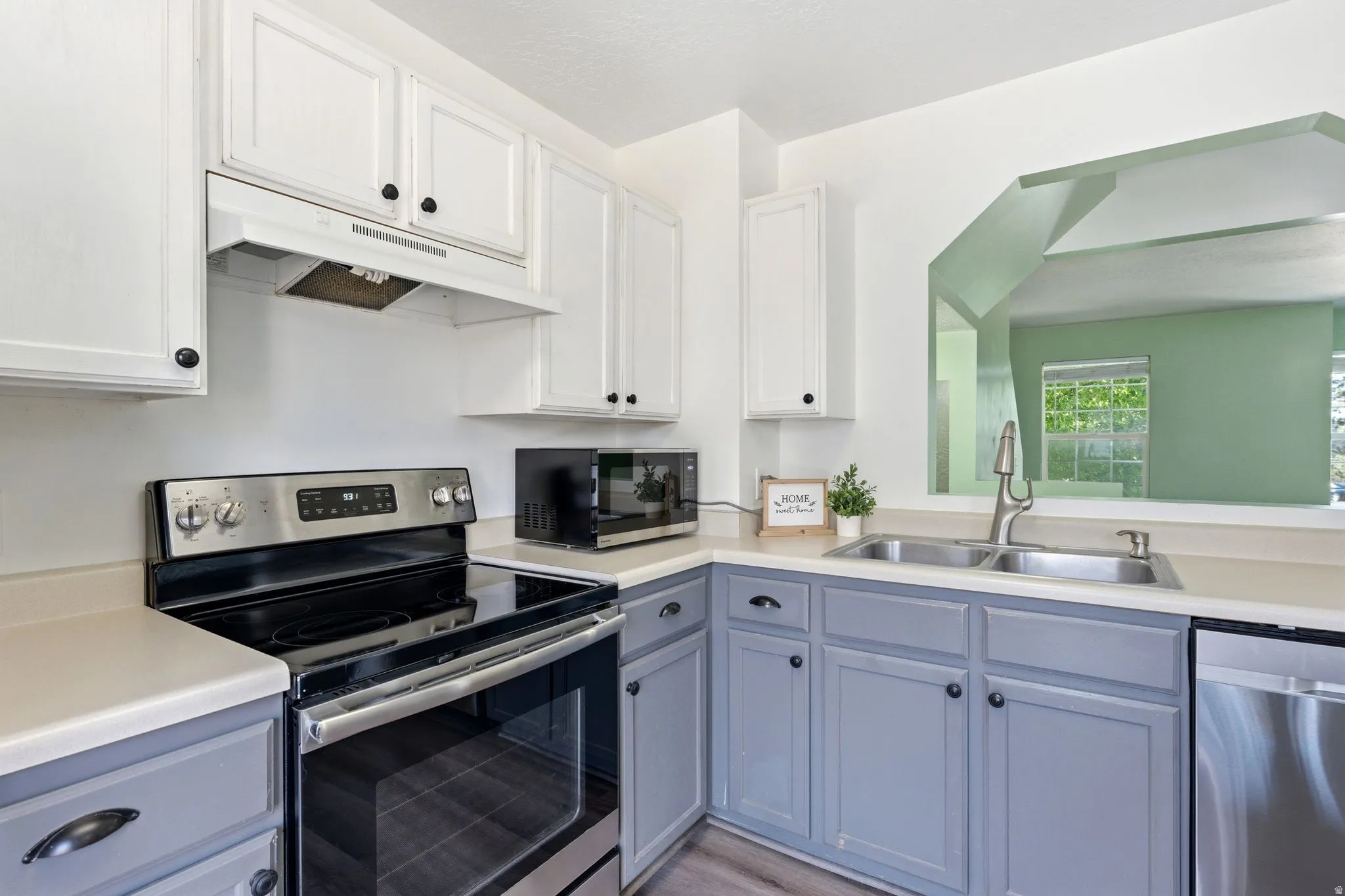 Kitchen featuring a stainless steel electric range, a double basin sink, light-toned countertops, two-tone cabinetry with black hardware, and an open pass-through window to an adjacent room