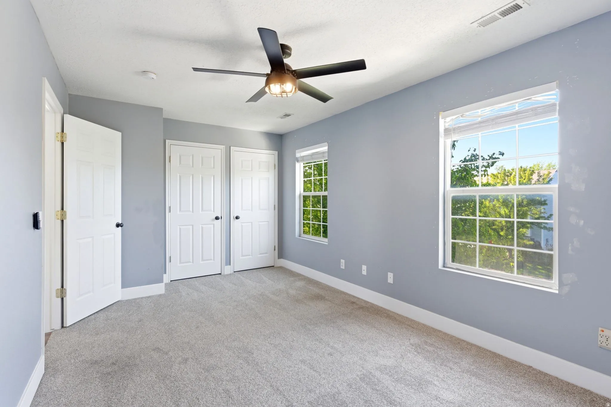 Carpeted room featuring light gray walls, two windows, and a ceiling fan with integrated lighting