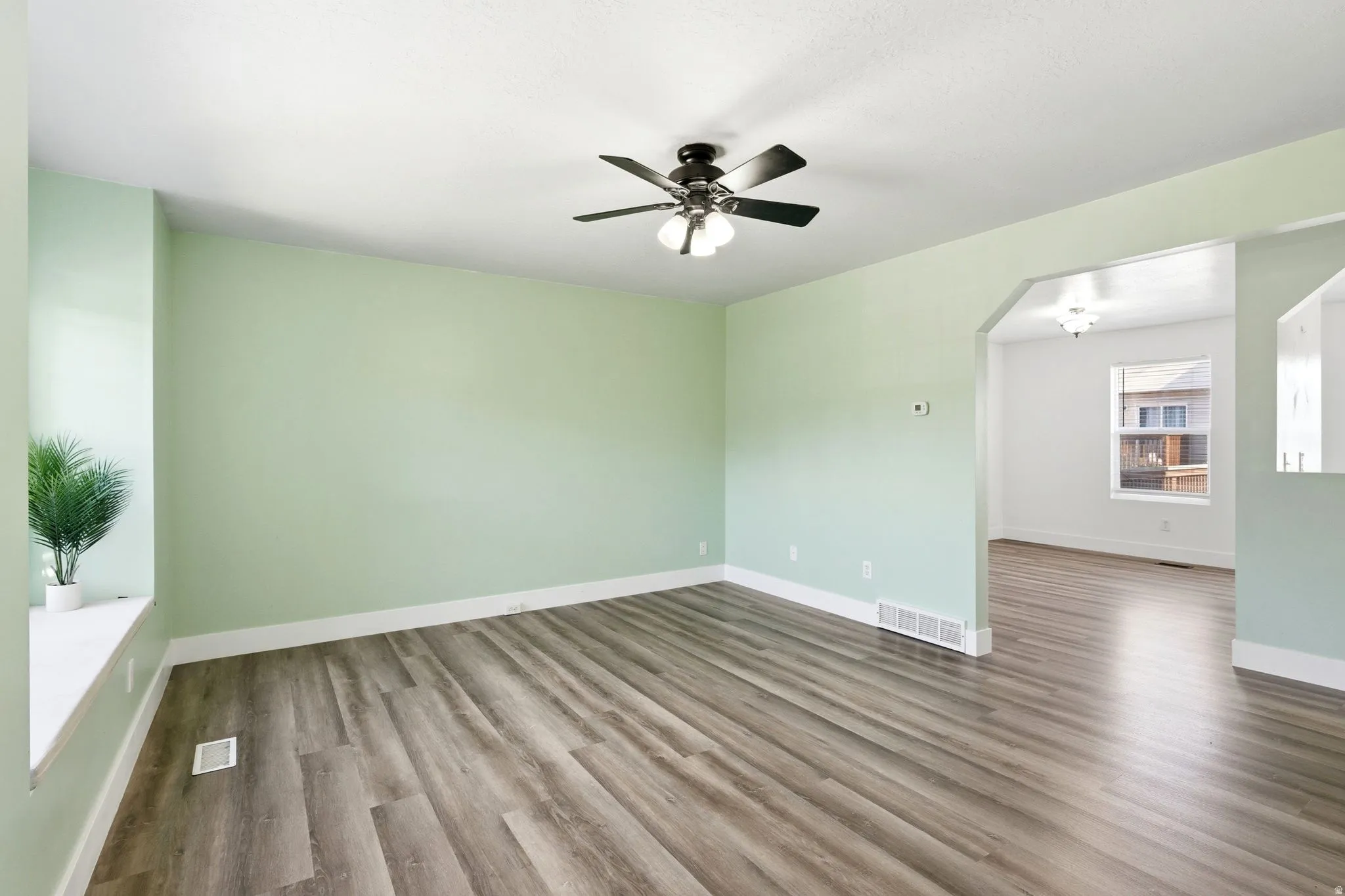Spacious room featuring wood-finish flooring, a ceiling fan with integrated lighting, and an arched doorway opening to an additional area