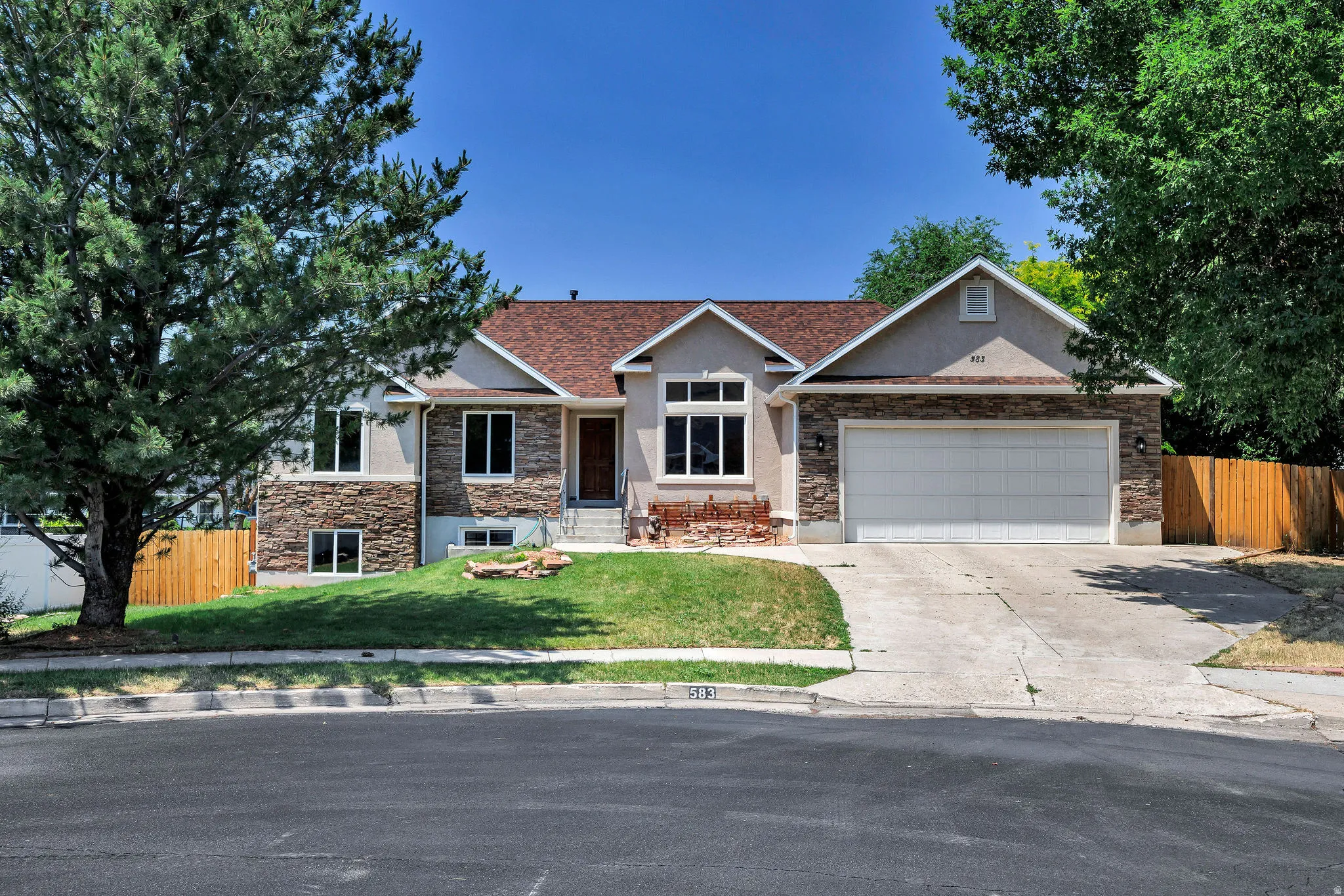 Split-level residence featuring a stucco and stone veneer facade, a two-car garage, and a concrete driveway