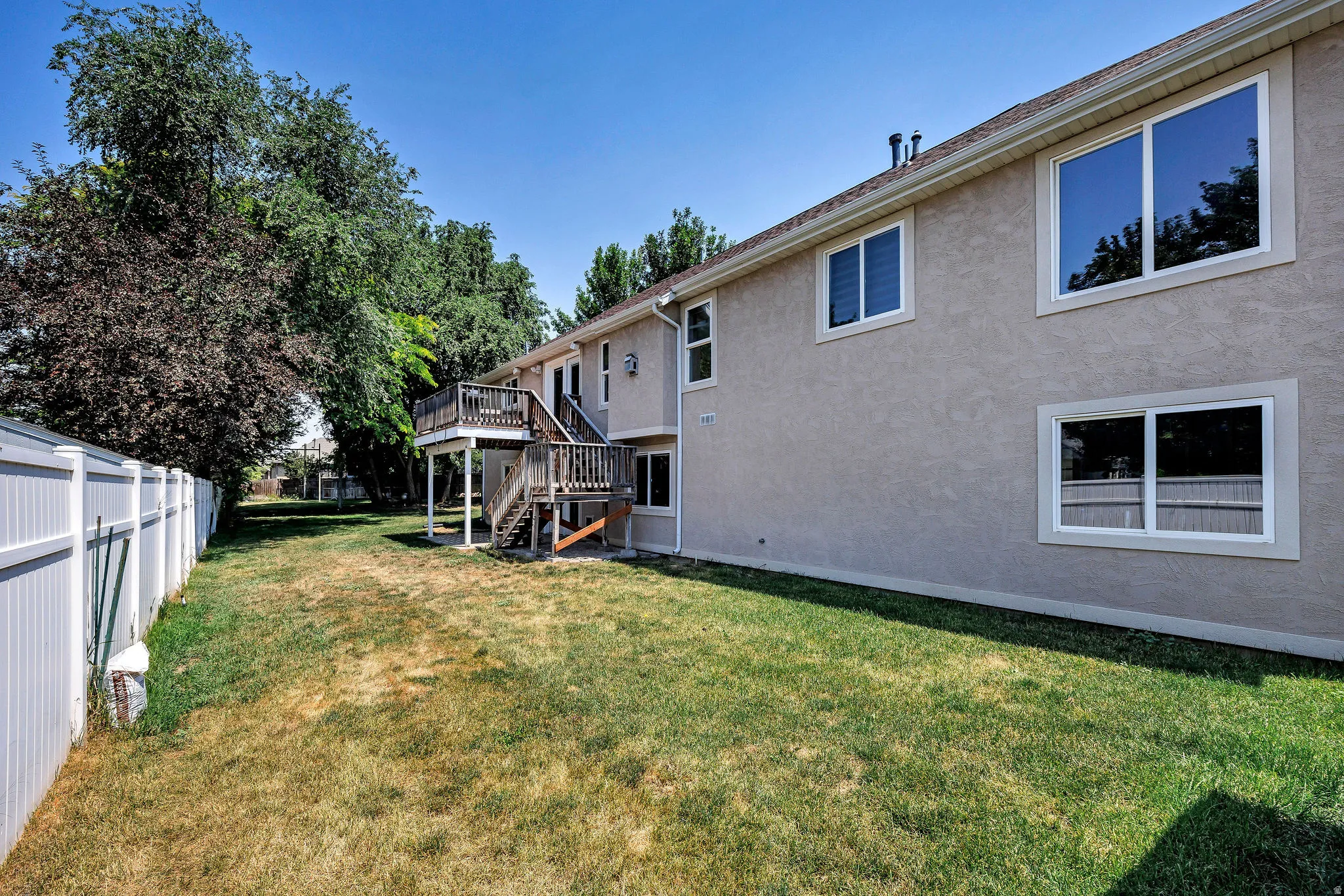 Rear exterior featuring a two-story wooden deck with stairs, a stucco facade, and multiple windows with white trim