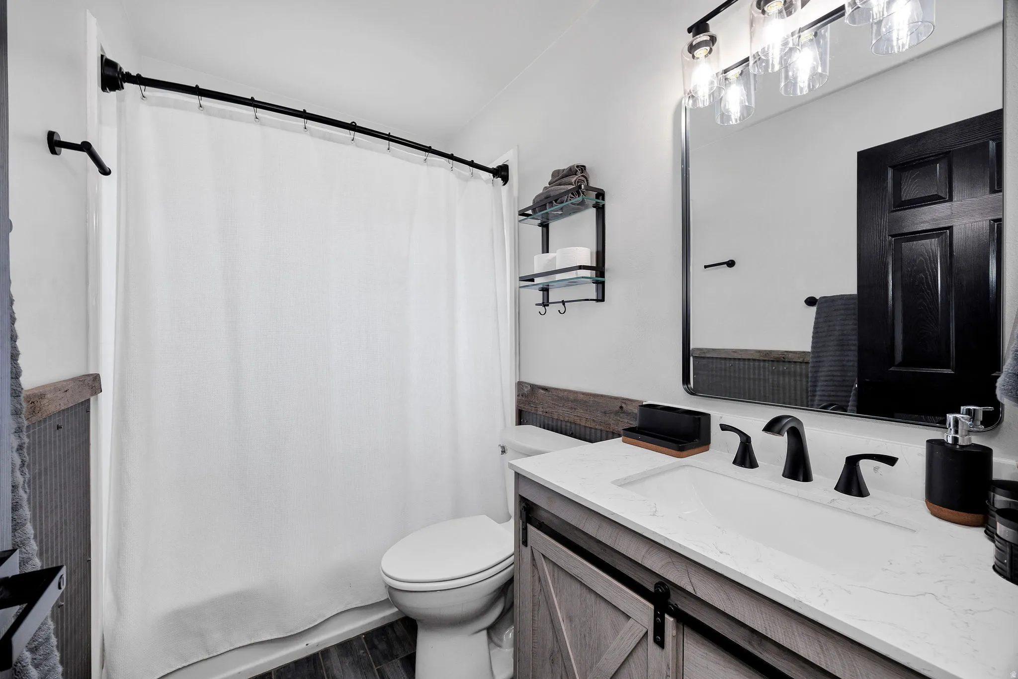 Bathroom featuring a shower-tub combination with a curved rod, a vanity with a barn door style cabinet, a white countertop with an integrated sink, a rectangular framed mirror, and a three-light vanity fixture
