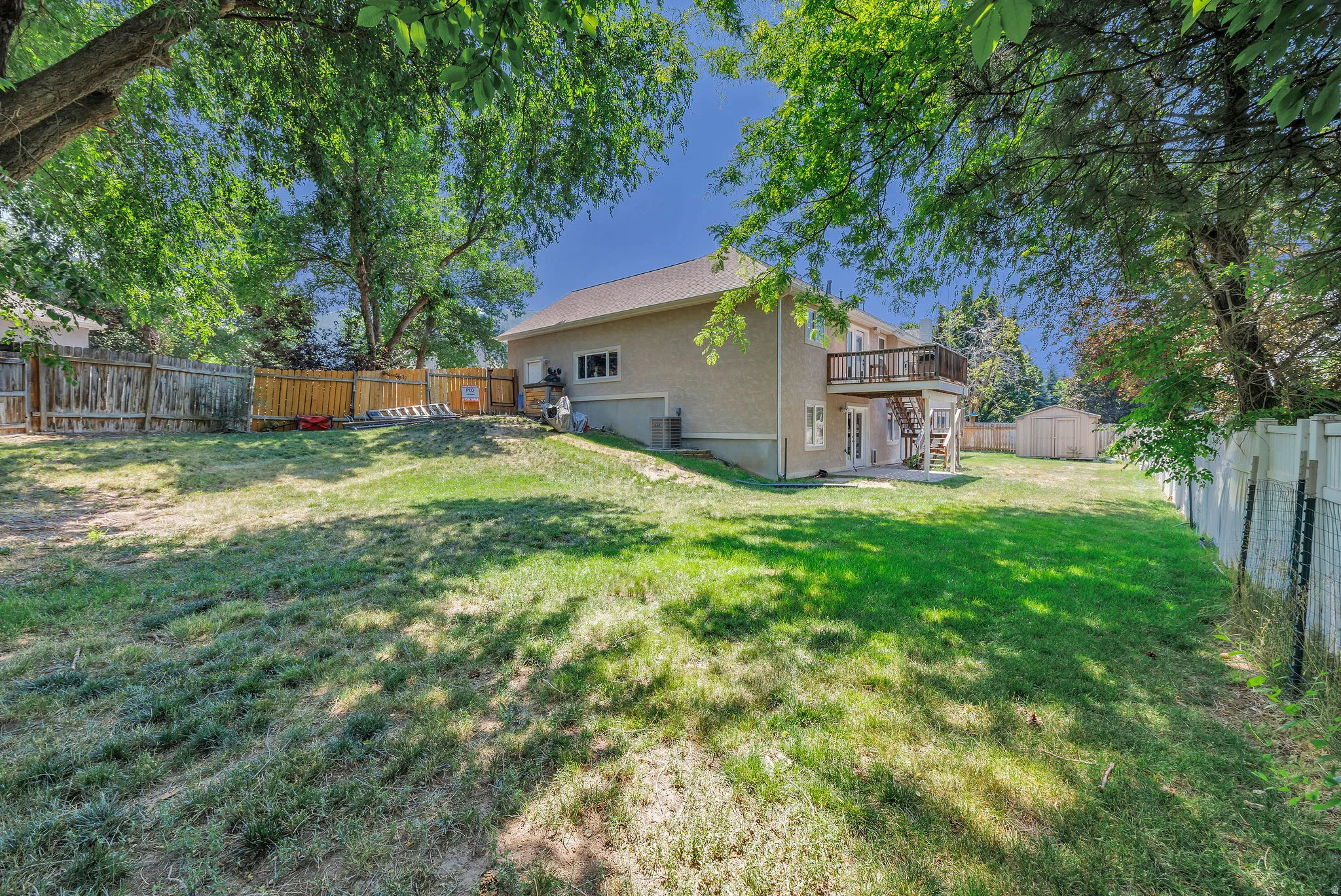 Expansive backyard featuring a multi-level deck, ground-level patio, mature trees, and a storage shed