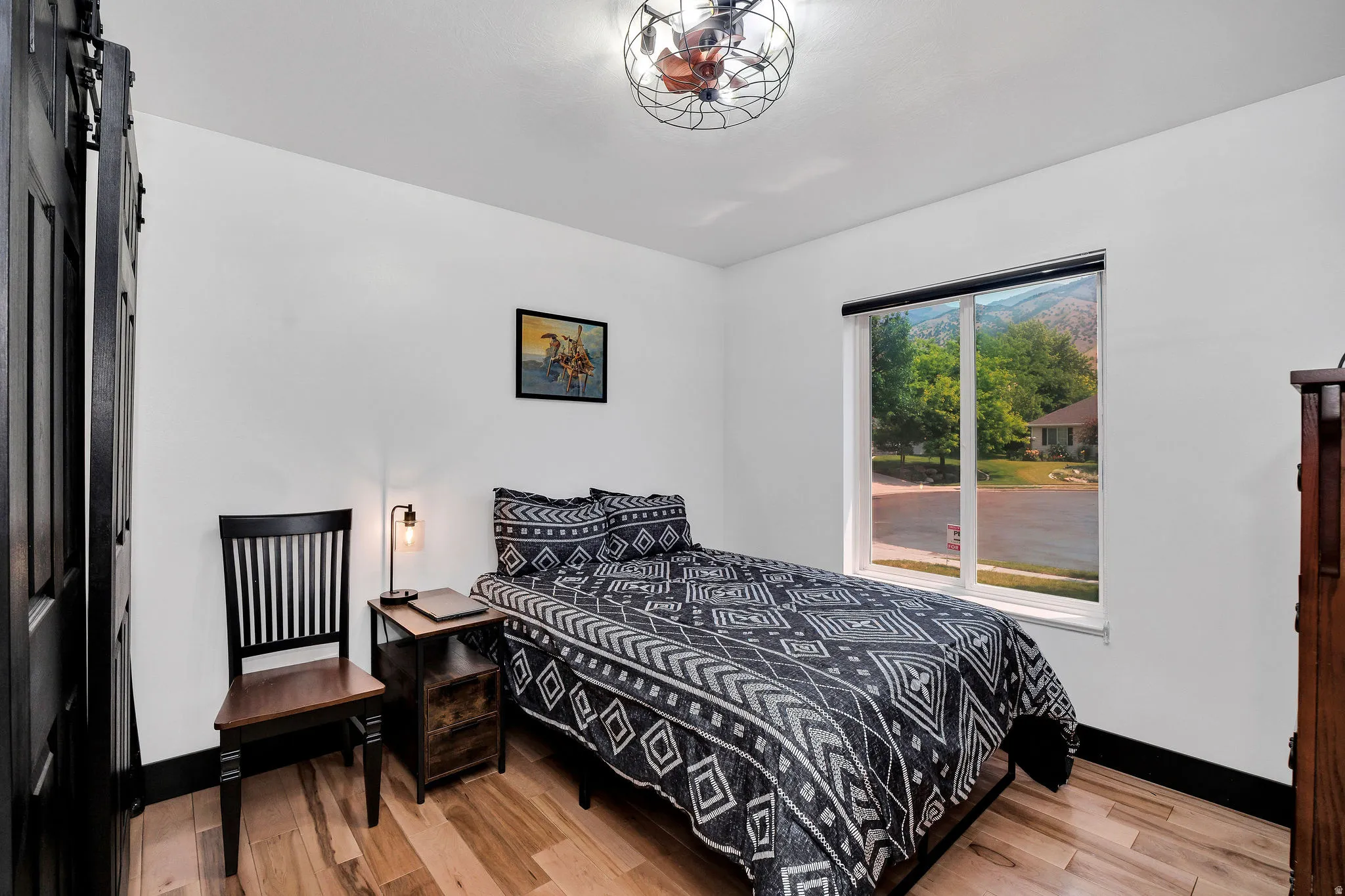 Bright room featuring a large window, a ceiling fan with integrated lighting, wood-finish flooring, white walls, and dark trim