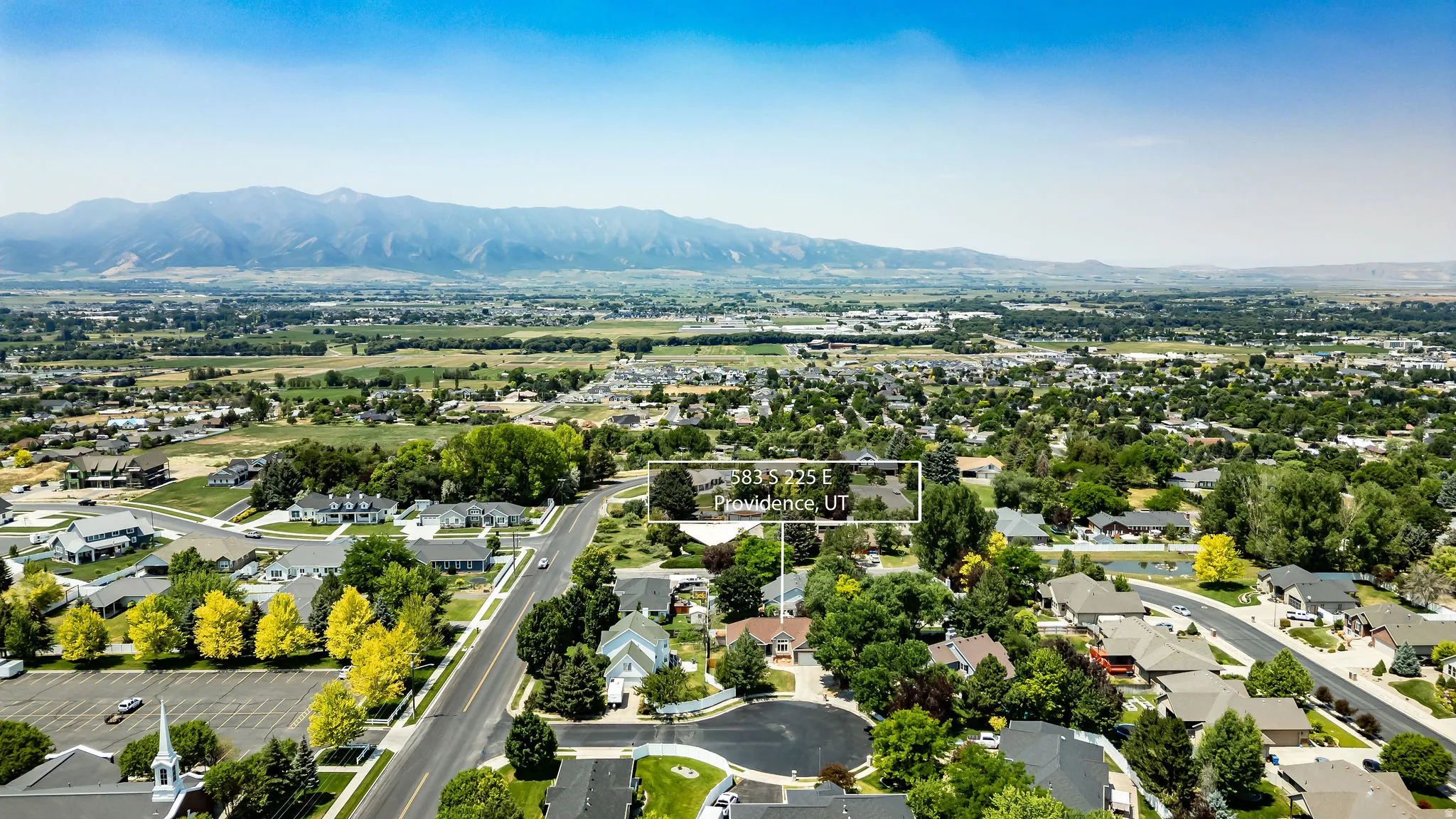 Aerial perspective of a residential community featuring established homes, mature trees, and a prominent roadway