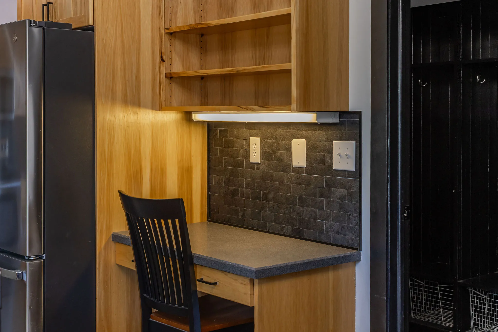 Built-in desk area featuring wood cabinetry, open shelving, integrated under-cabinet lighting, a tiled backsplash, and a solid surface countertop