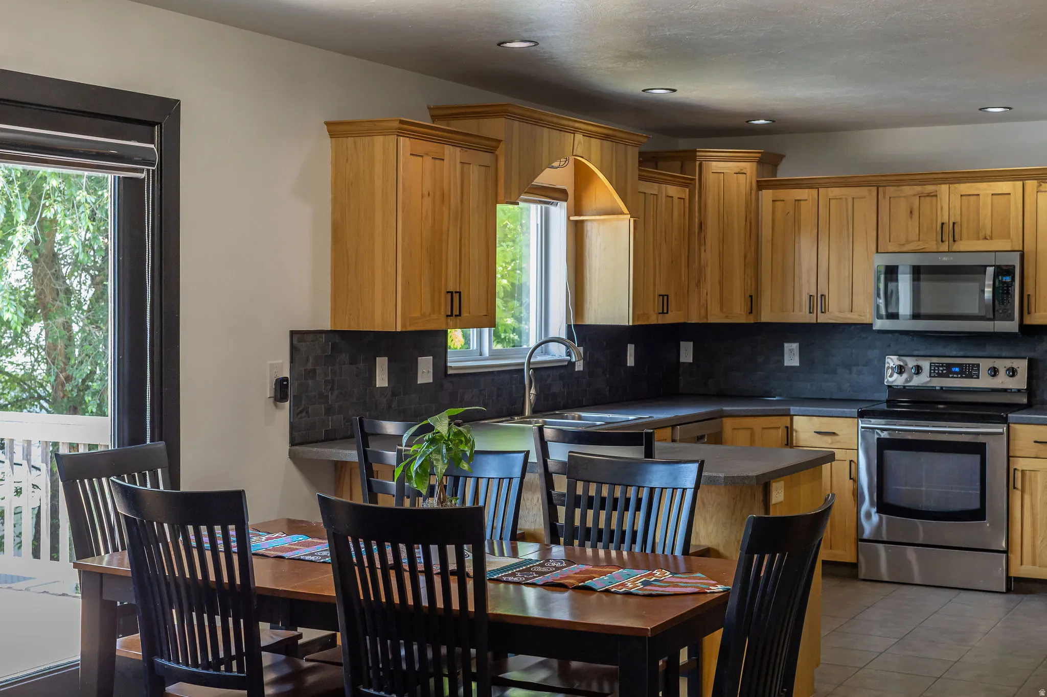 Kitchen featuring wood-finish cabinetry, stainless steel appliances, dark subway tile backsplash, and recessed lighting