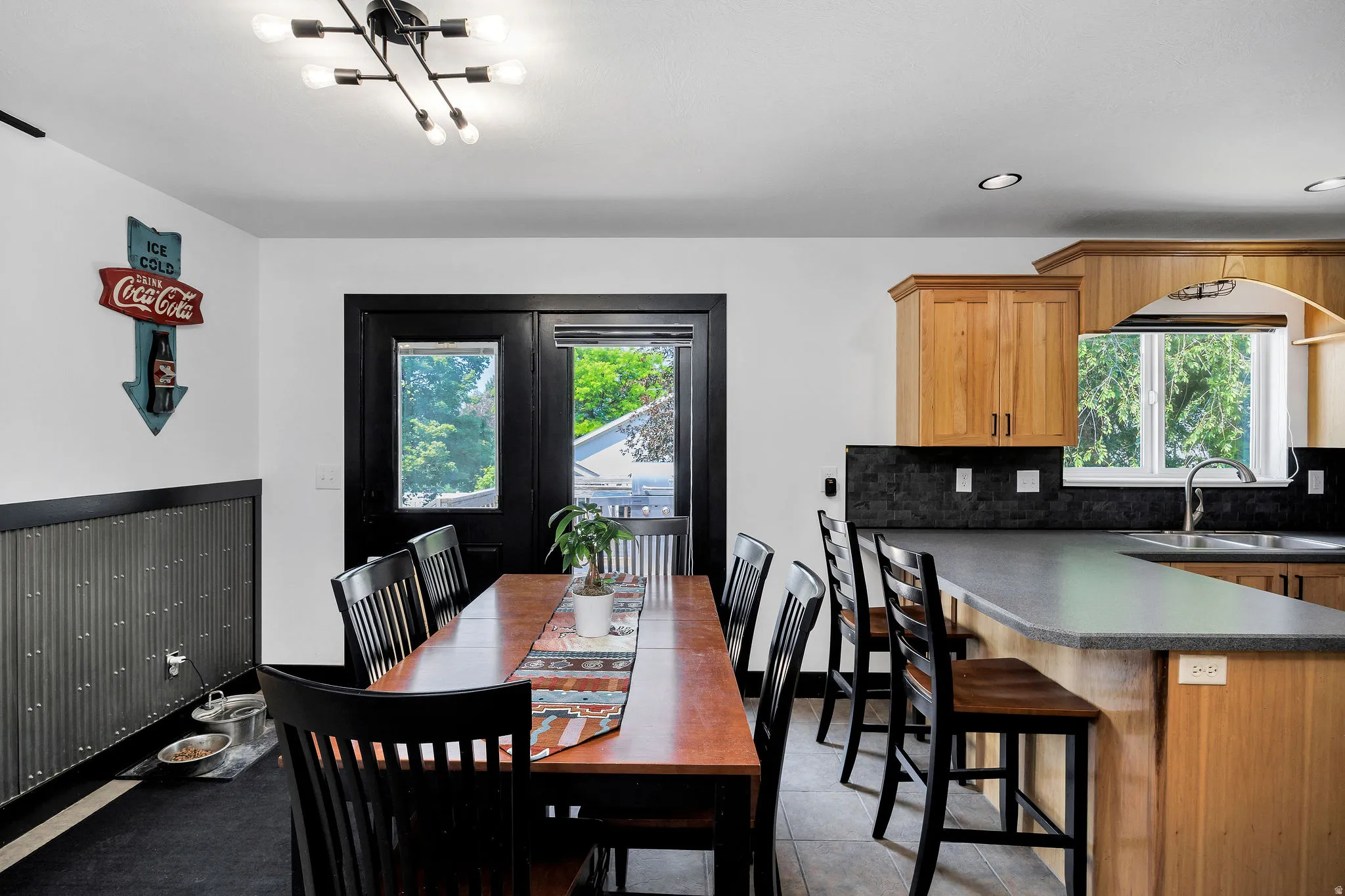 Open concept dining area and kitchen featuring wood-finish cabinetry, dark countertops, and a black tile backsplash