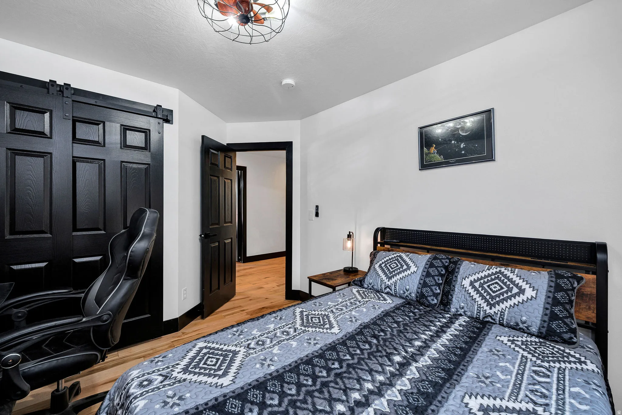 Bedroom featuring light-tone wood-finish flooring, a black paneled barn door, and a black paneled interior door