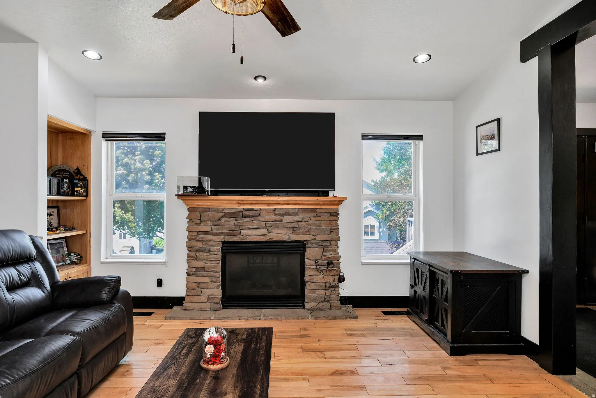 Living space featuring a stone-clad fireplace with a wood mantel, overhead recessed lighting, and wood-finish flooring