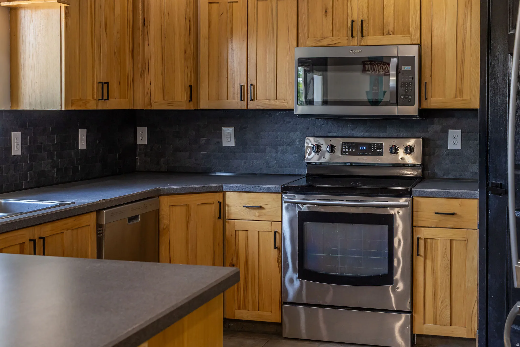 Kitchen featuring wood cabinetry with black hardware, dark countertops, and a dark subway tile backsplash