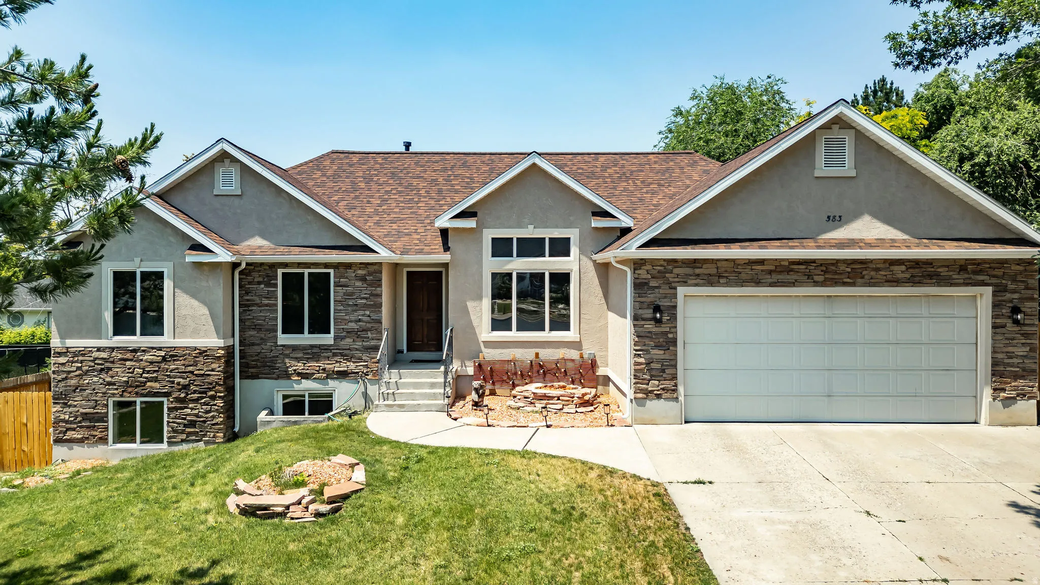 Contemporary residence featuring a brown shingle roof, light stucco, and stacked stone facade