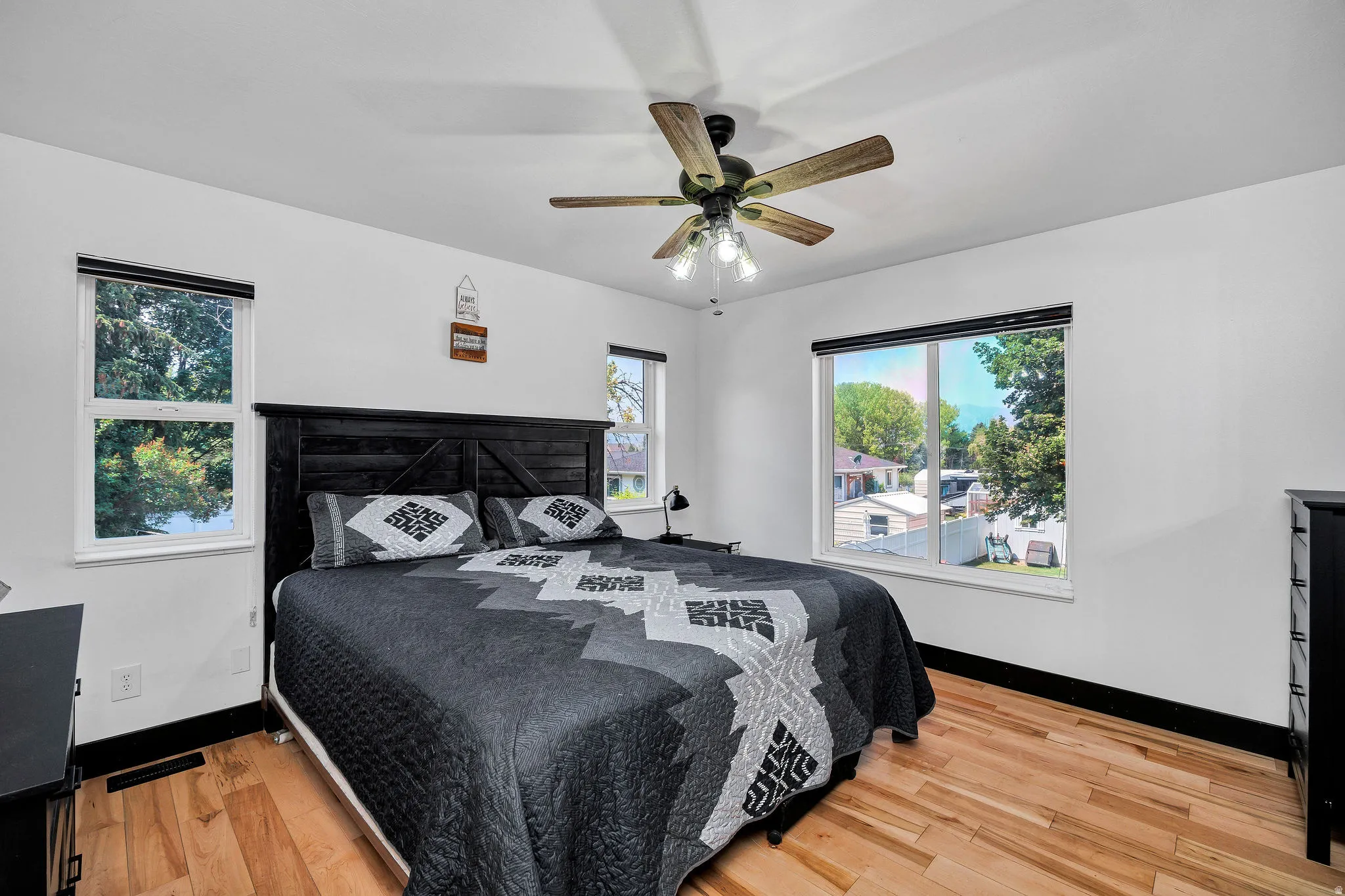 Spacious room featuring light wood-finish flooring, white walls, and a multi-blade ceiling fan with integrated lighting