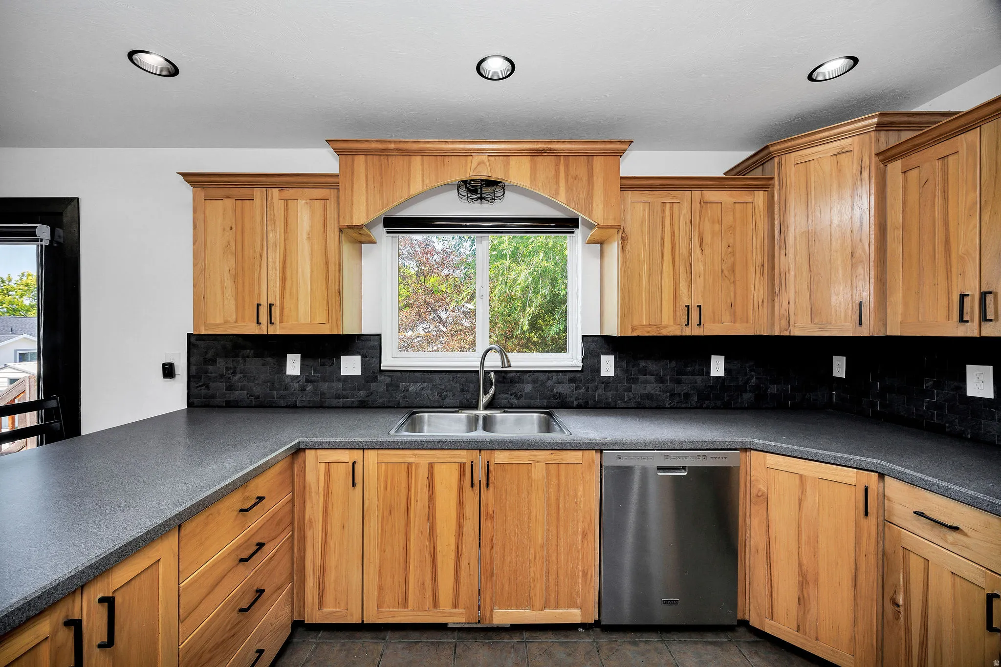 Kitchen featuring abundant wood cabinetry, dark countertops, a tile backsplash, stainless steel sink, and recessed ceiling lighting