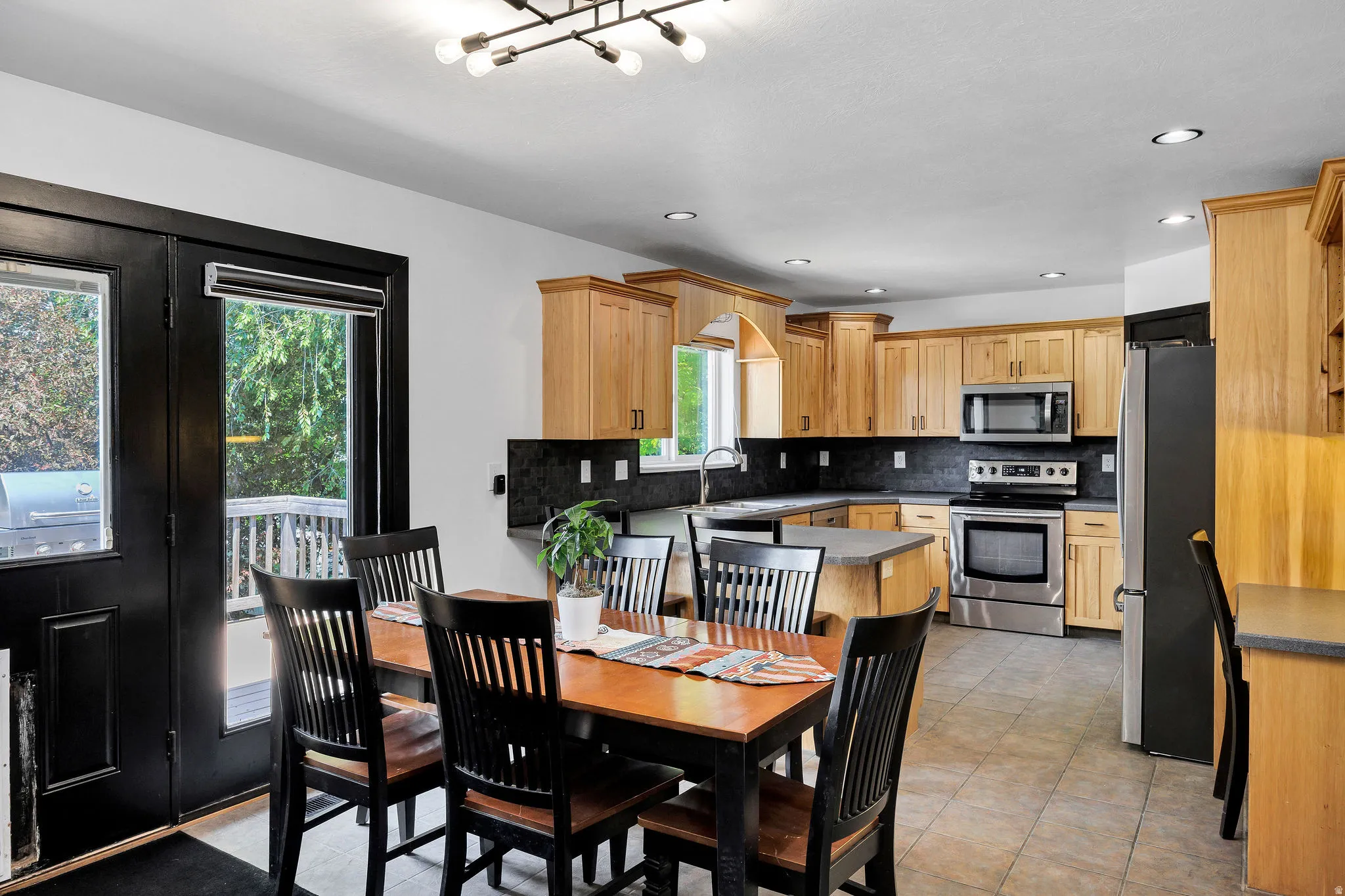 Kitchen featuring light wood cabinetry, stainless steel appliances, dark stone countertops, tile flooring, and recessed lighting