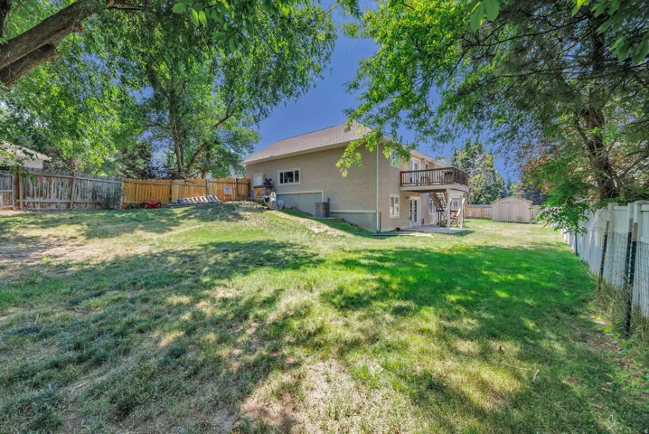 Expansive backyard featuring a multi-level deck, ground-level patio, mature trees, and a storage shed