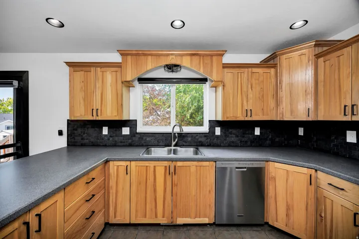 Kitchen featuring abundant wood cabinetry, dark countertops, a tile backsplash, stainless steel sink, and recessed ceiling lighting